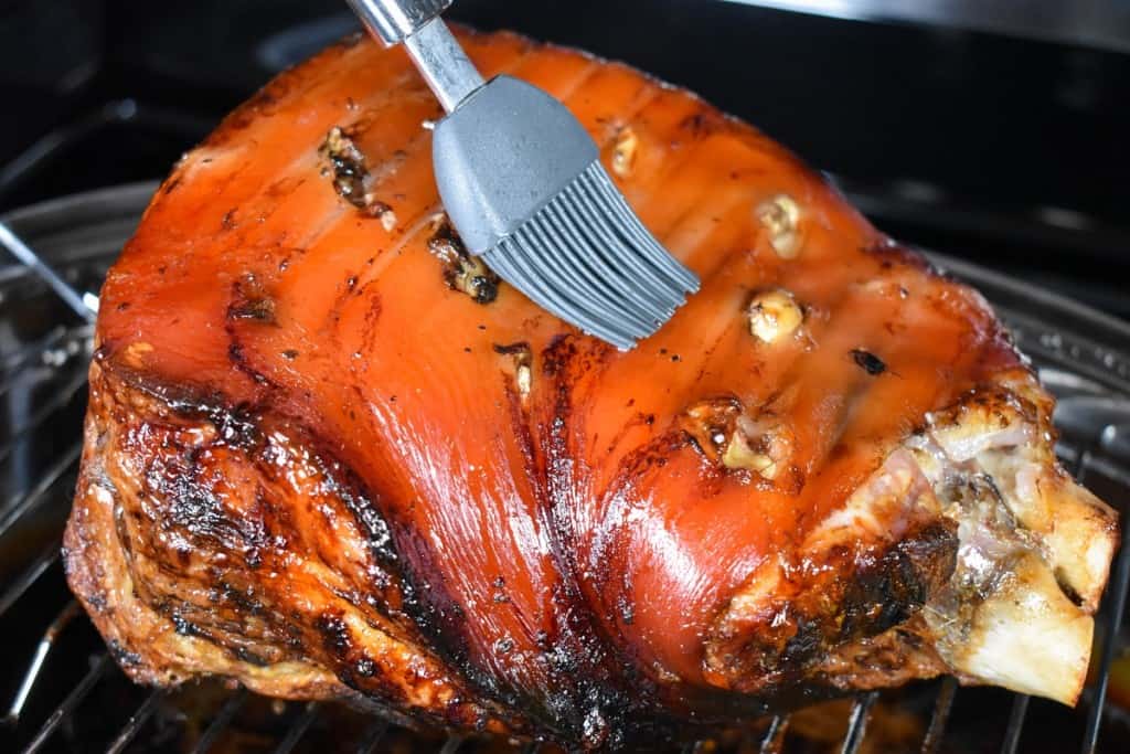 An image of a cooked pork shoulder with a gray silicone brush adding water to the top.