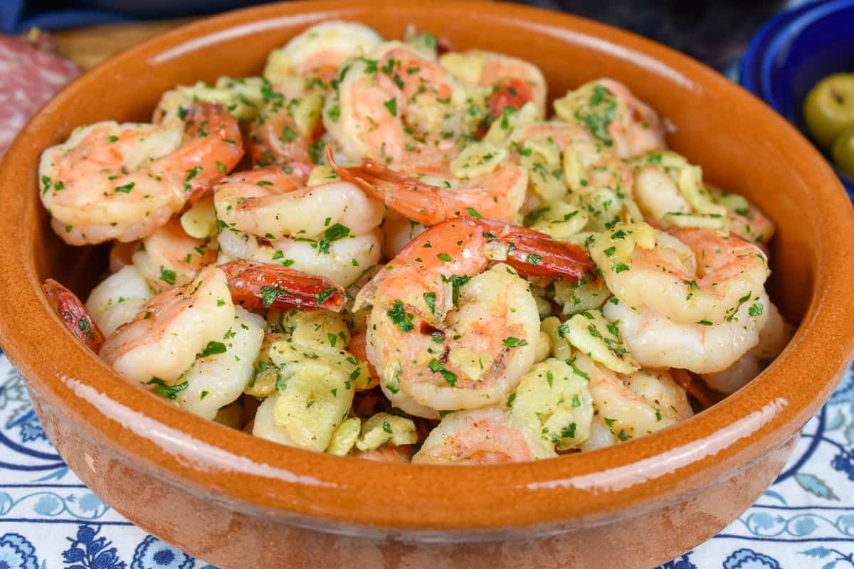 A close up image of camarones al ajillo served in an orange, clay bowl.