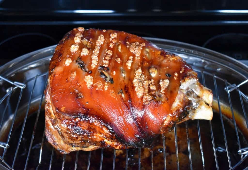 An image of the pork shoulder skin side up on the rack of a large roasting pan.