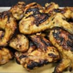 Grilled chicken wings with golden and caramelized skin piled on a sheet pan