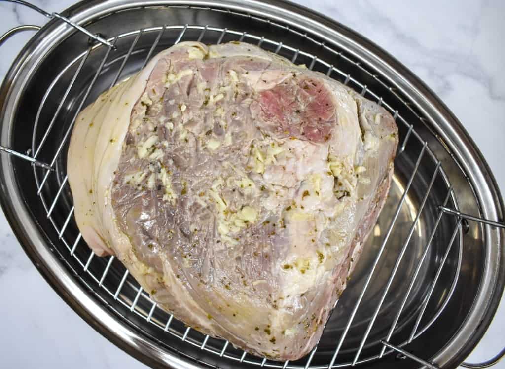 A marinated pork shoulder set on a large roasting pan with a rack. The meat is a soft grayish color.