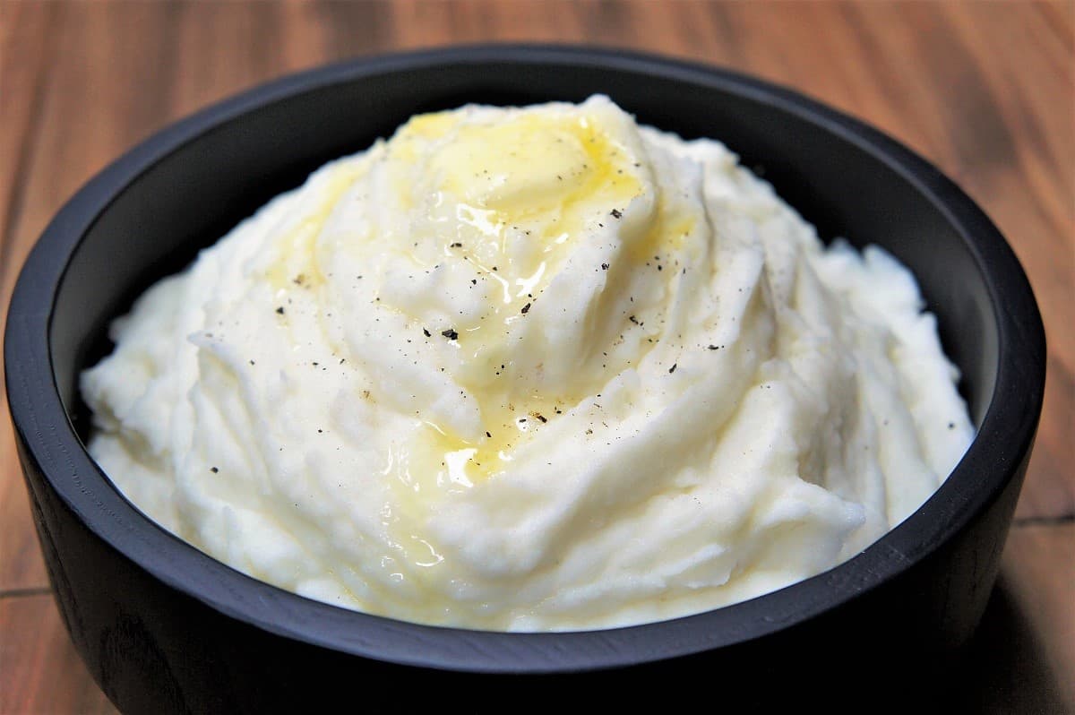 Mashed potatoes in a black bowl with a pat of melting butter on top.