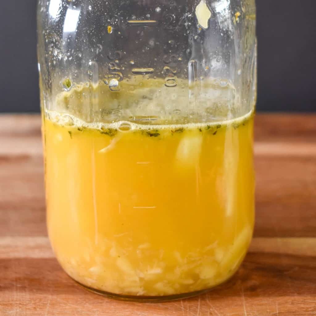 An image of mojo marinade in a large canning jar set on a wood cutting board.