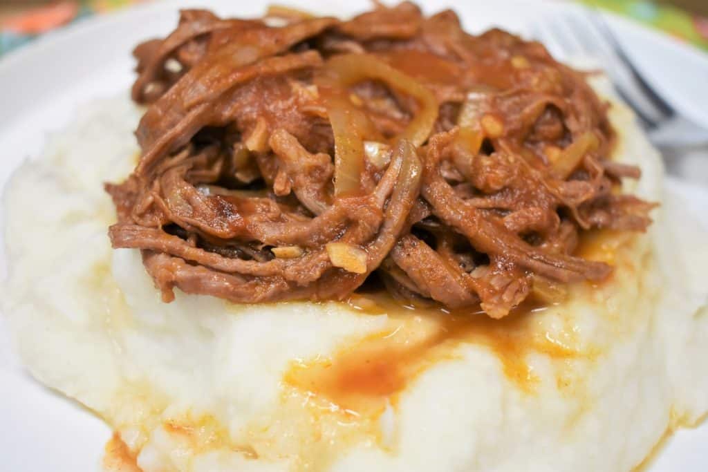 Ropa vieja served on a bed of mashed malanga on a white plate.