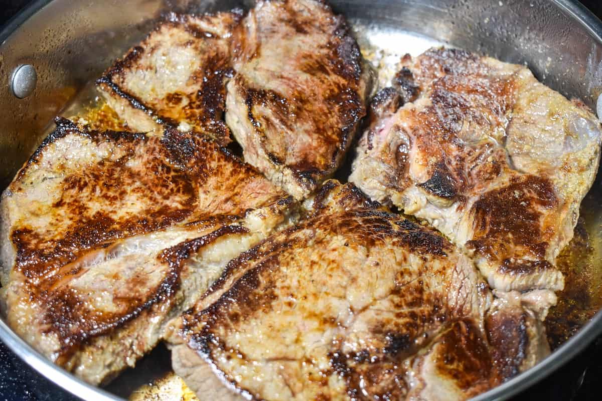 Four thick steaks arranged on a large skillet with the seared part up.