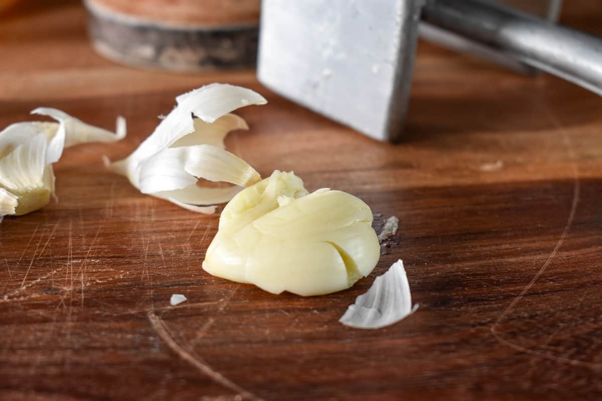 A smashed garlic clove on a wood cutting board.