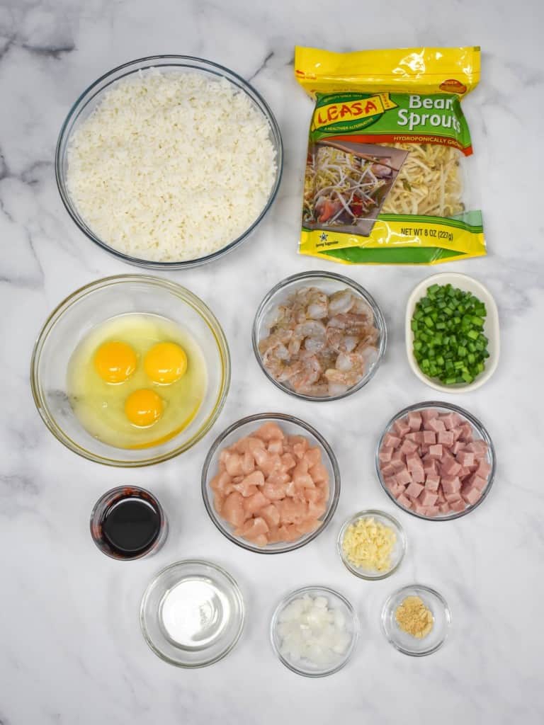The prepped ingredients for the fried rice arranged in separate bowls on a white table. The bean sprouts are in their package.