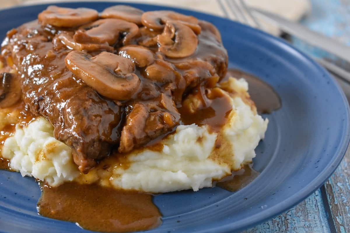 A close up image of the steak with mushrooms on a bed of mashed potatoes served on a blue plate.