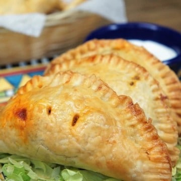 Taco Hand Pies three small hand pies on a colorful plate on a bed of shredded lettuce with hot sauce and sour cream on the side