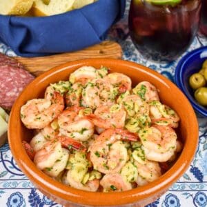 Camarones al ajillo served in a terracotta colored bowl on a blue and white linen.