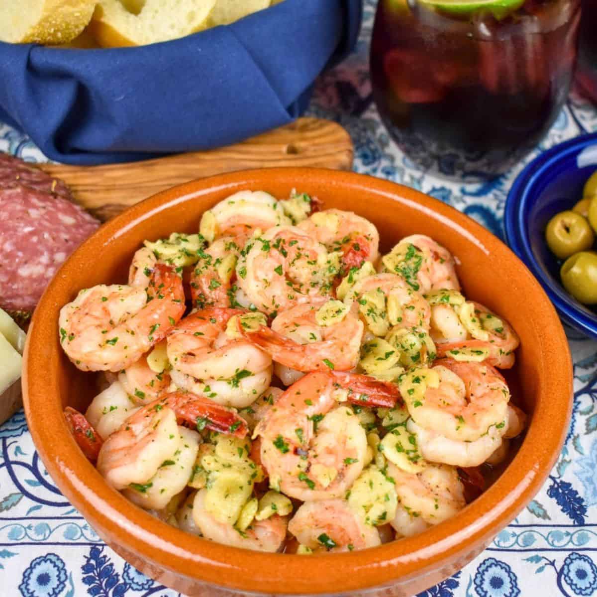 Camarones al ajillo served in a terracotta colored bowl on a blue and white linen.