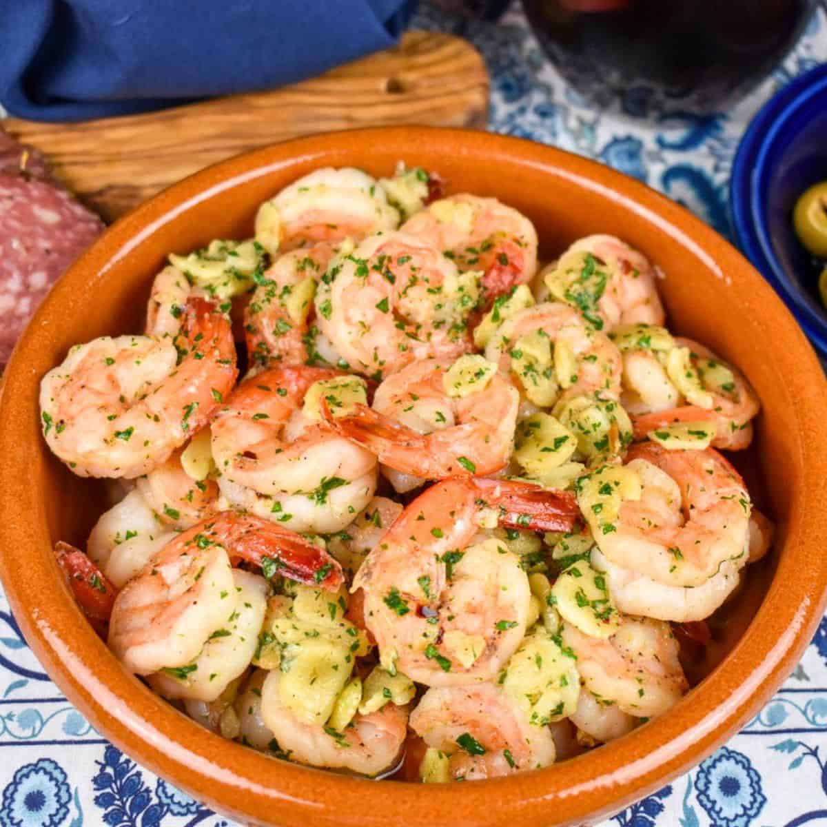 Camarones al ajillo served in a terracotta colored bowl on a blue and white linen.