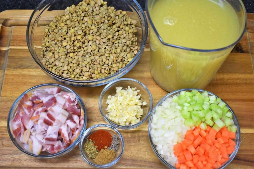 The ingredients for this bacon and lentil soup displayed on a wood cutting board.