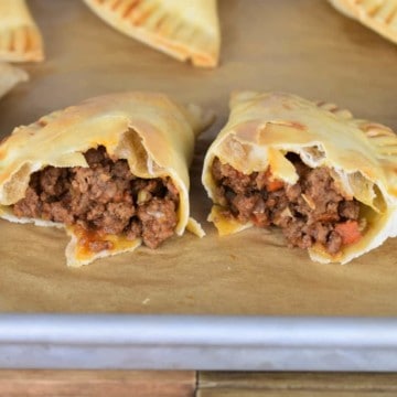 Baked Beef Empanadas on a baking sheet with one cut in half exposing the beef filling