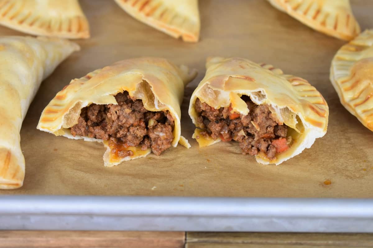 Baked Beef Empanadas on a baking sheet with one cut in half exposing the beef filling