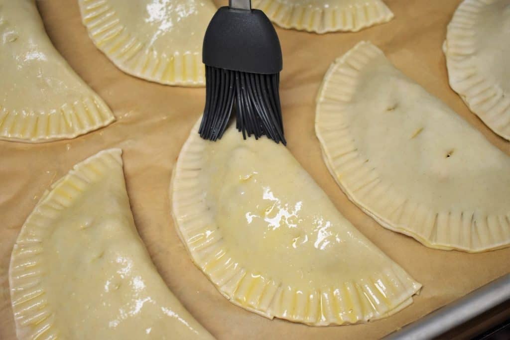 Brushing Egg Wash on Empanadas arranged on a baking sheet