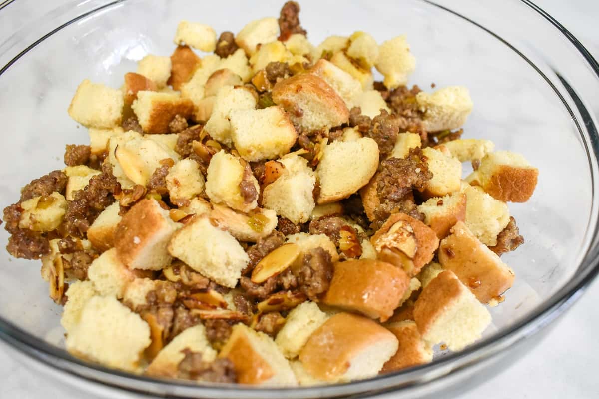 The sausage mixture with the croutons in a large glass bowl set on a white table.