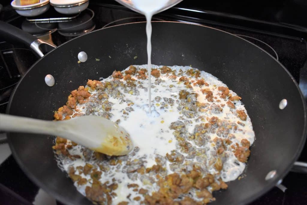 Half and half being added to a sausage mixture in a large, black skillet.