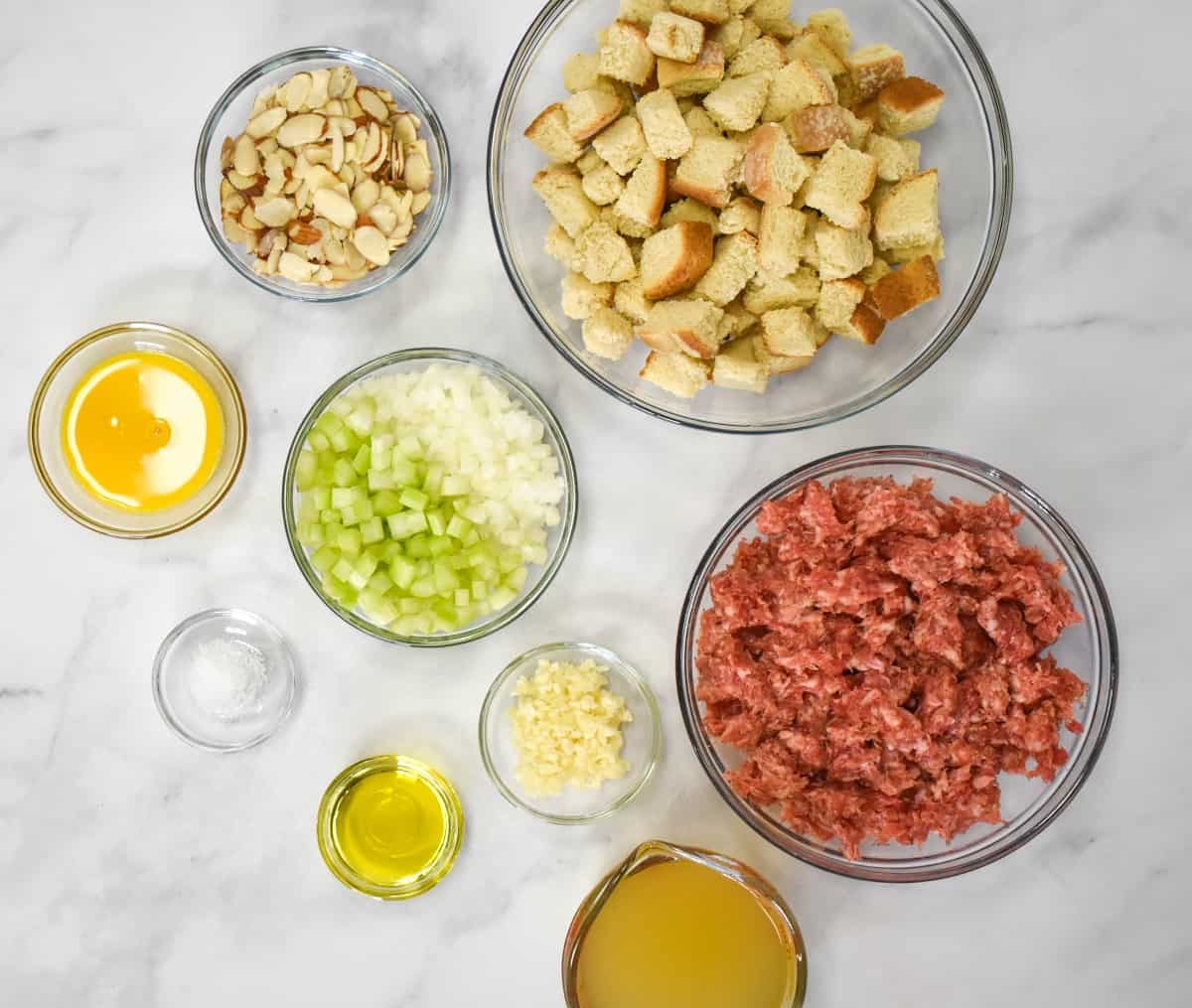 The ingredients for the sausage stuffing, prepped and arranged in glass bowls on a white table.