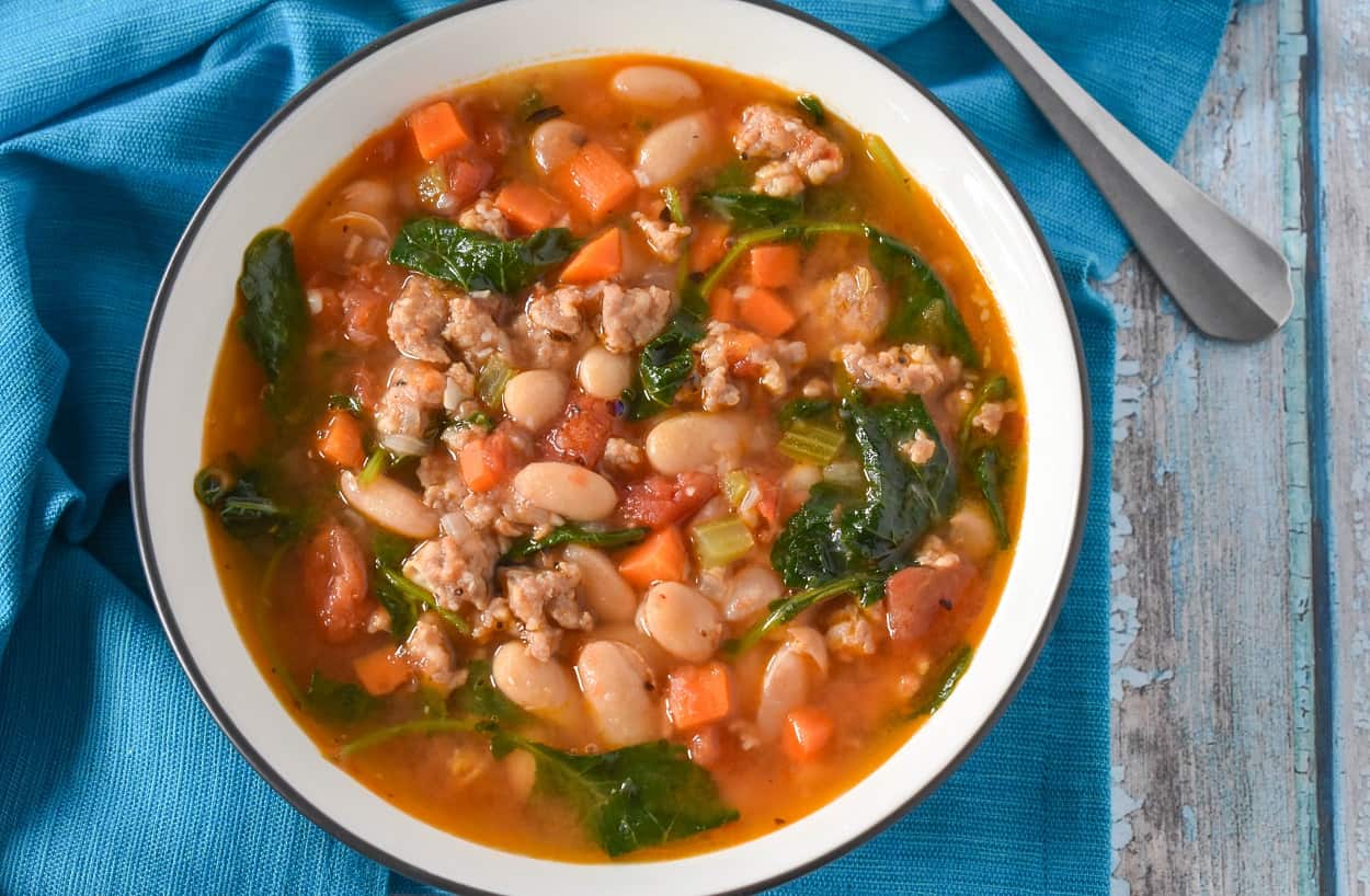 The sausage white bean soup served in a white bowl on a turquoise linen.