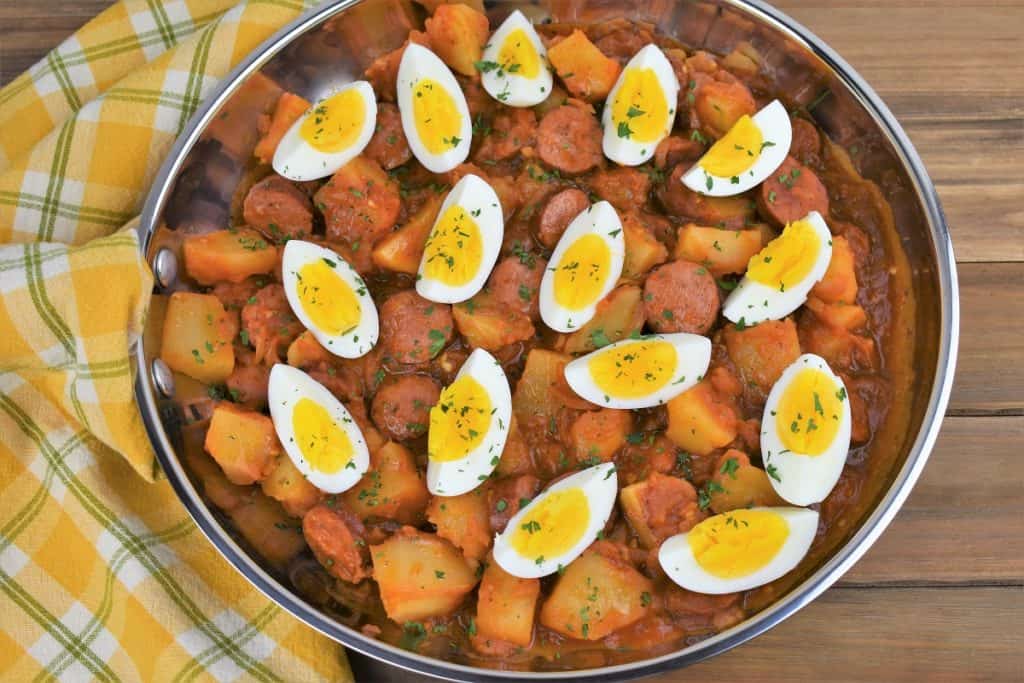Sausage and Potatoes in a skillet in tomato sauce and topped with quartered hard boiled eggs