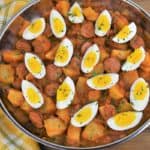 Sausage and Potatoes in a skillet in tomato sauce and topped with quartered hard boiled eggs