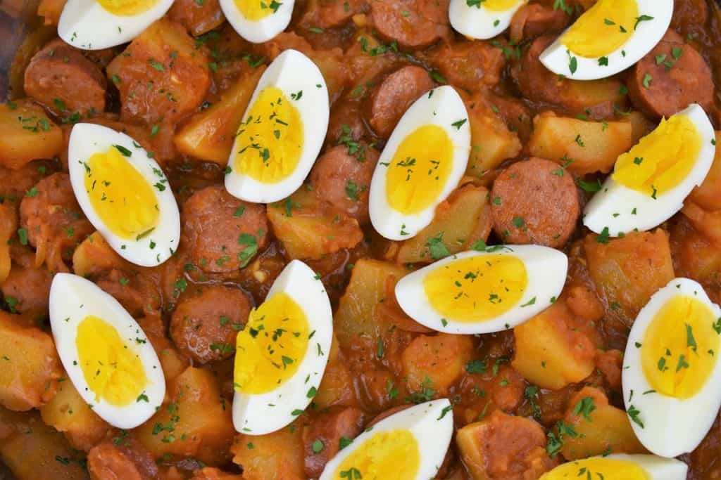 Close up picture of sausage and potatoes topped with quartered hard boiled eggs in a skillet