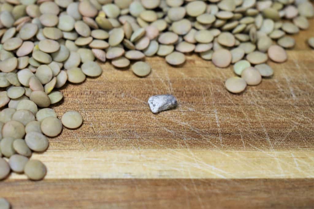 Lentils on a wood cutting board and a small stone that was found in the lentils.