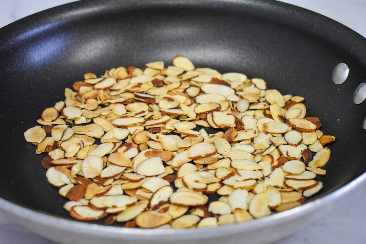 Sliced toasted almonds in a black, non stick skillet.