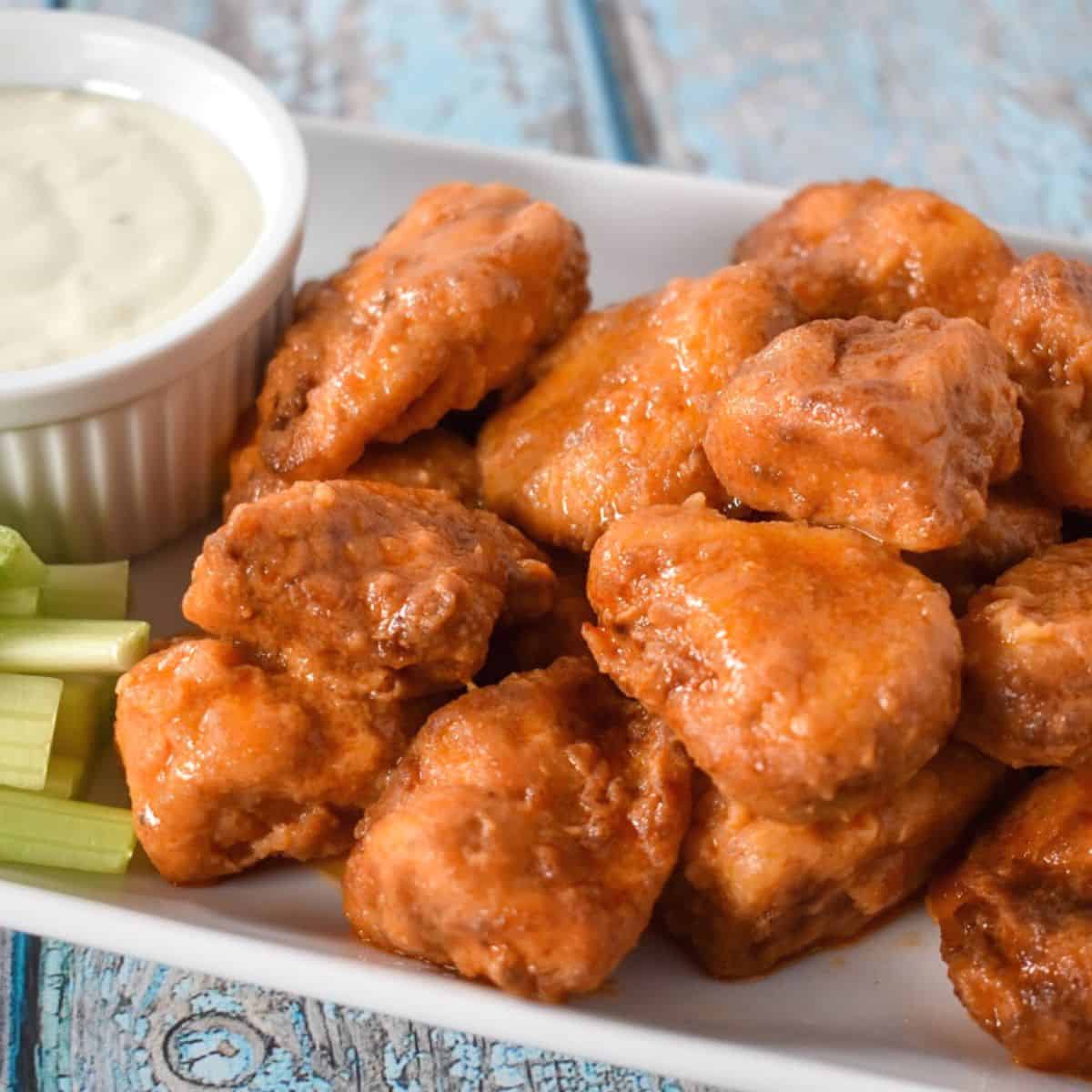 Buffalo chicken bites served on a white platter with a side of blue cheese dressing and celery sticks.