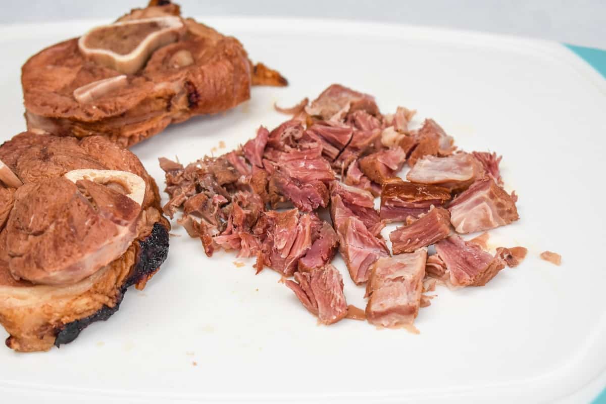 Ham shanks on a white cutting board with bones removed and chopped.