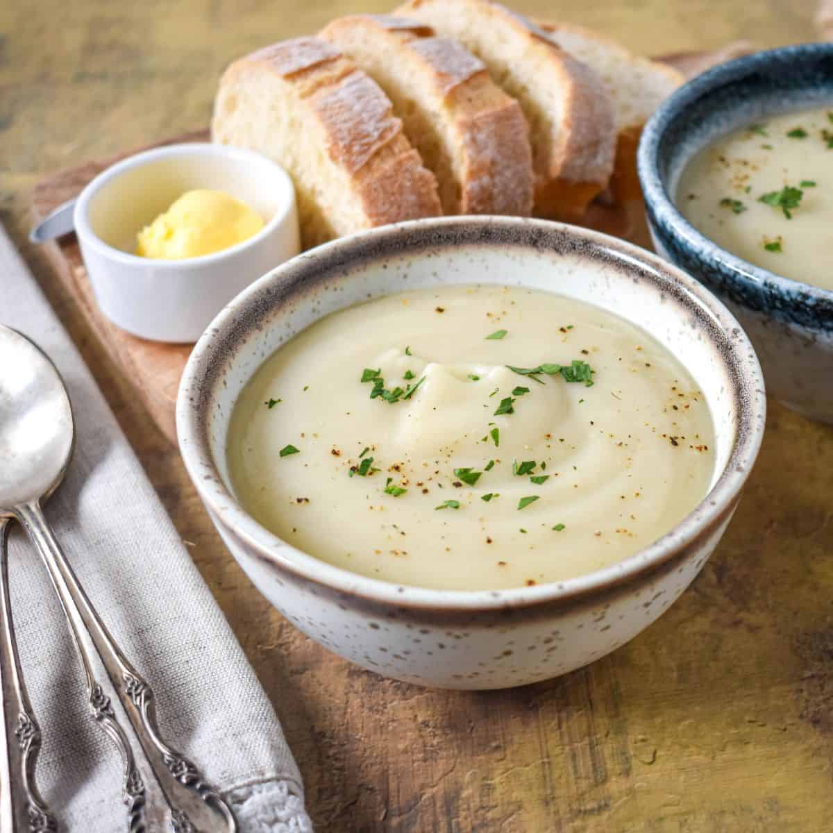 A bowl of crema de malanga garnished with parsley, served with sliced bread and a small dish of butter.