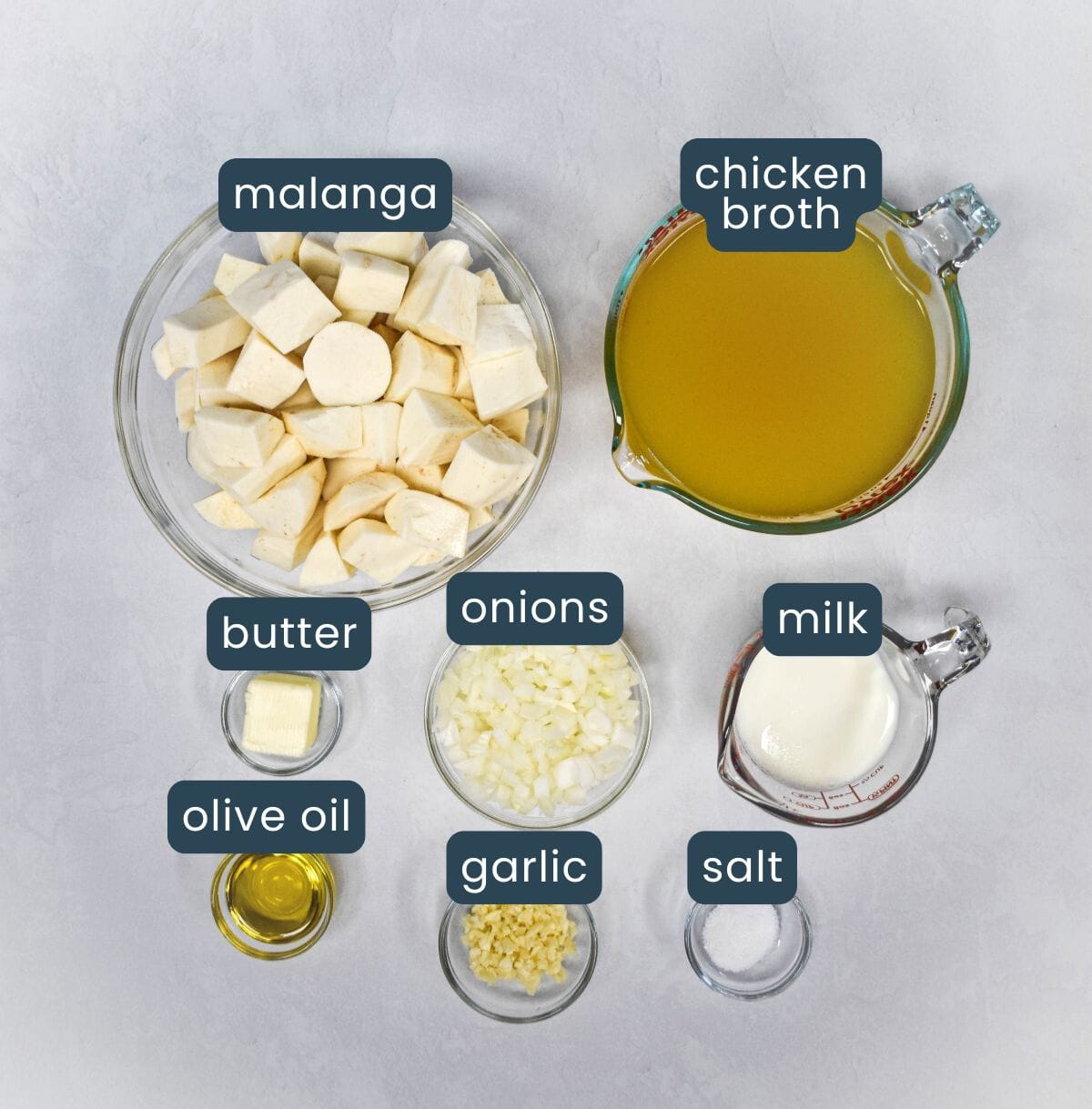 Overhead view of labeled, prepped ingredients for making the soup, including malanga root, broth, aromatics, and milk.