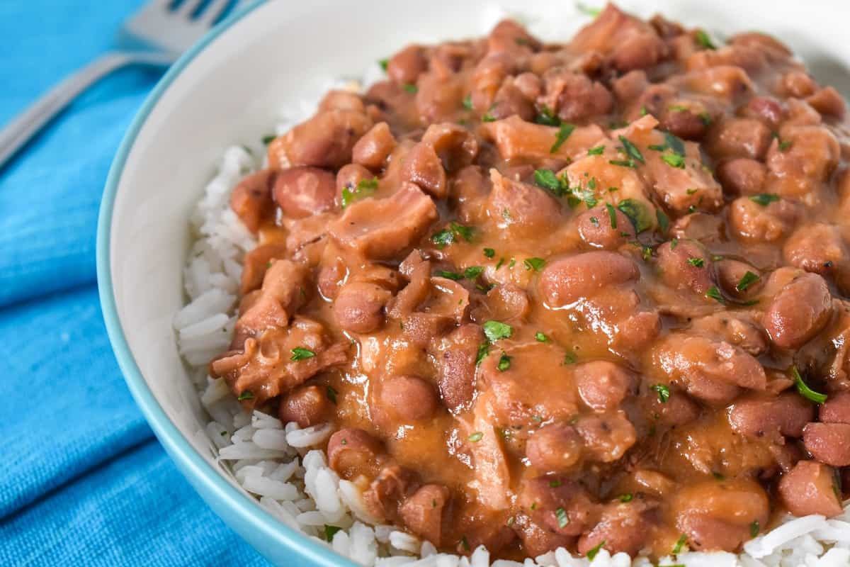 A close-up of the beans served over white rice in a white bowl on an aqua linen.