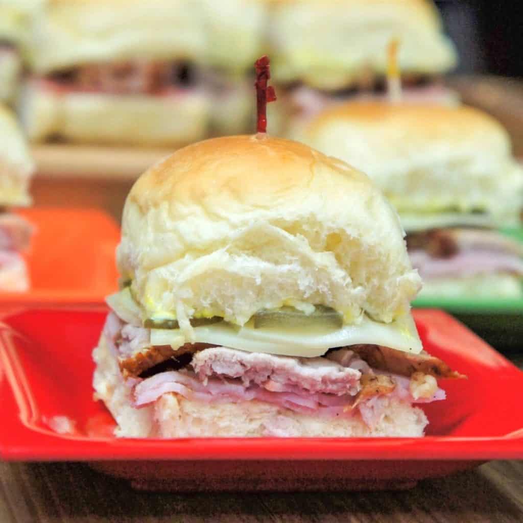 A close up of a Cuban slider on a small red plate with other sliders in the background.