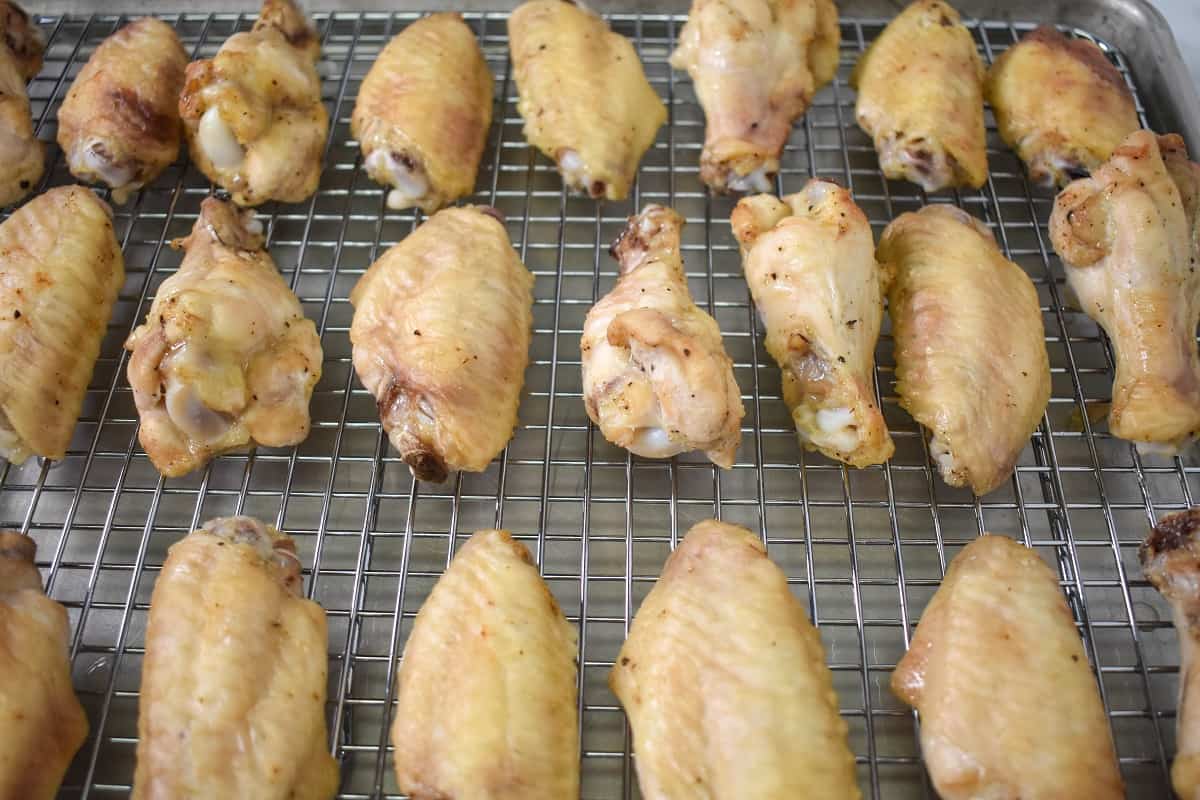 The half-baked wings arranged on a large baking sheet that's lined with a cooling rack.