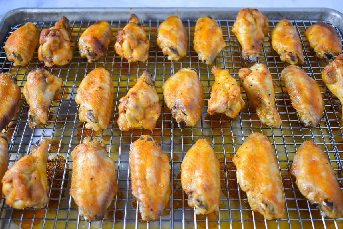 The finished buffalo wings arranged on a large baking sheet that's lined with a cooling rack.