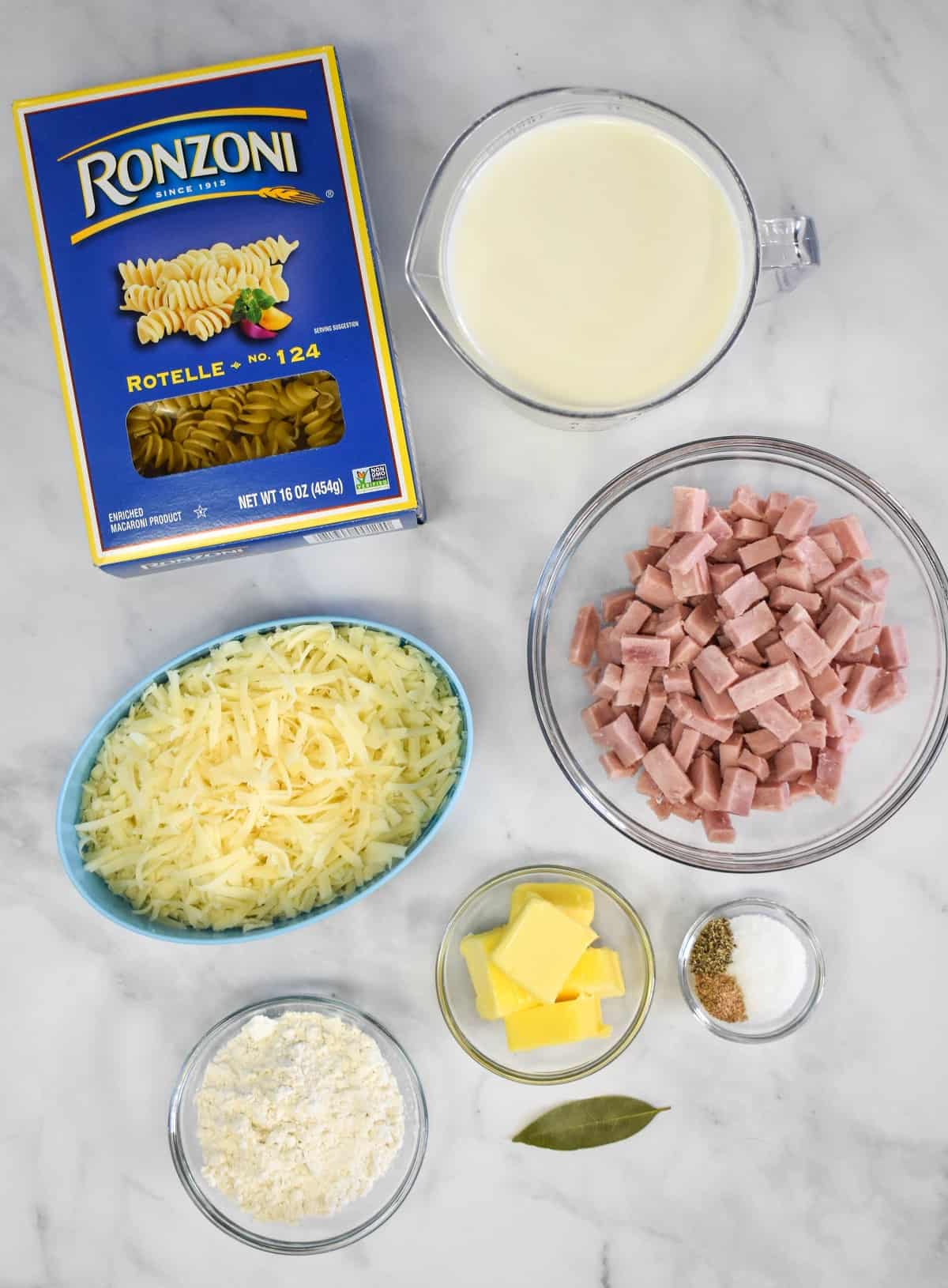 The prepped ingredients for the ham and cheese pasta arranged in separate containers on a white table.