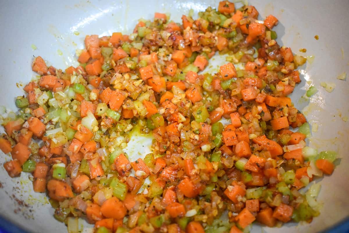 Diced onions, carrots, celery, tomato paste, and spices combined and being cooked in a large pot.