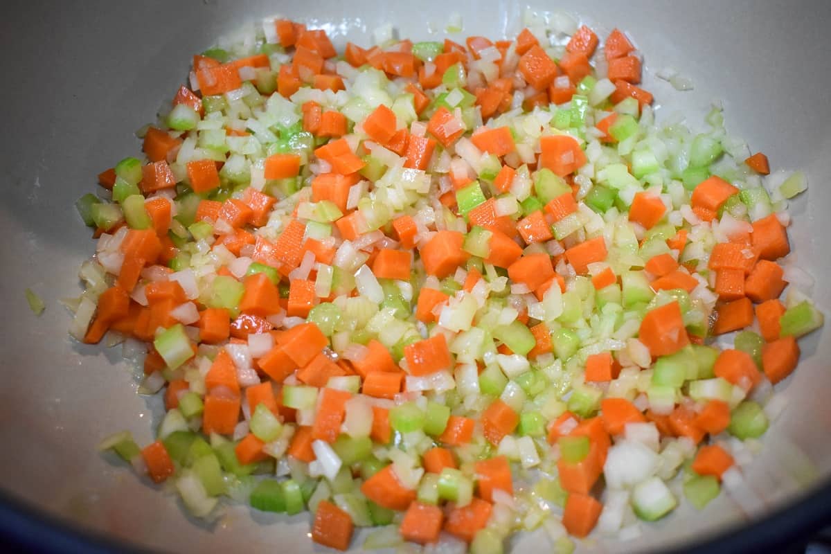 Diced onions, carrots and celery being cooked in olive oil in a large pot.