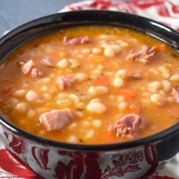 Navy bean soup served in a black bowl, with a red and white cloth napkin and spoon on the side.