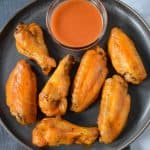 Seven chicken wings arranged on a gray plate with a side of buffalo sauce in a small bowl.