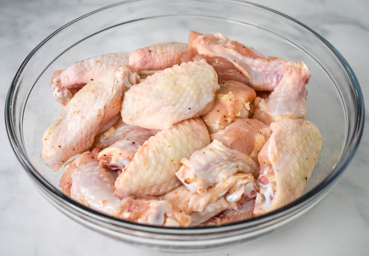 The seasoned wings in a large clear bowl.