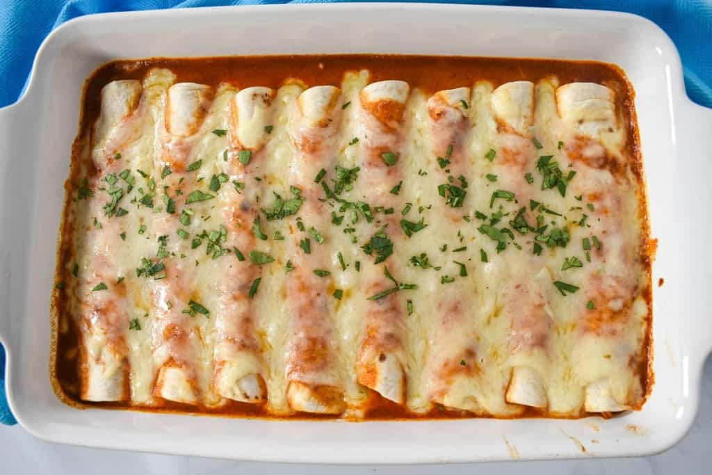 An image of the chicken enchiladas after baking in a white casserole dish.