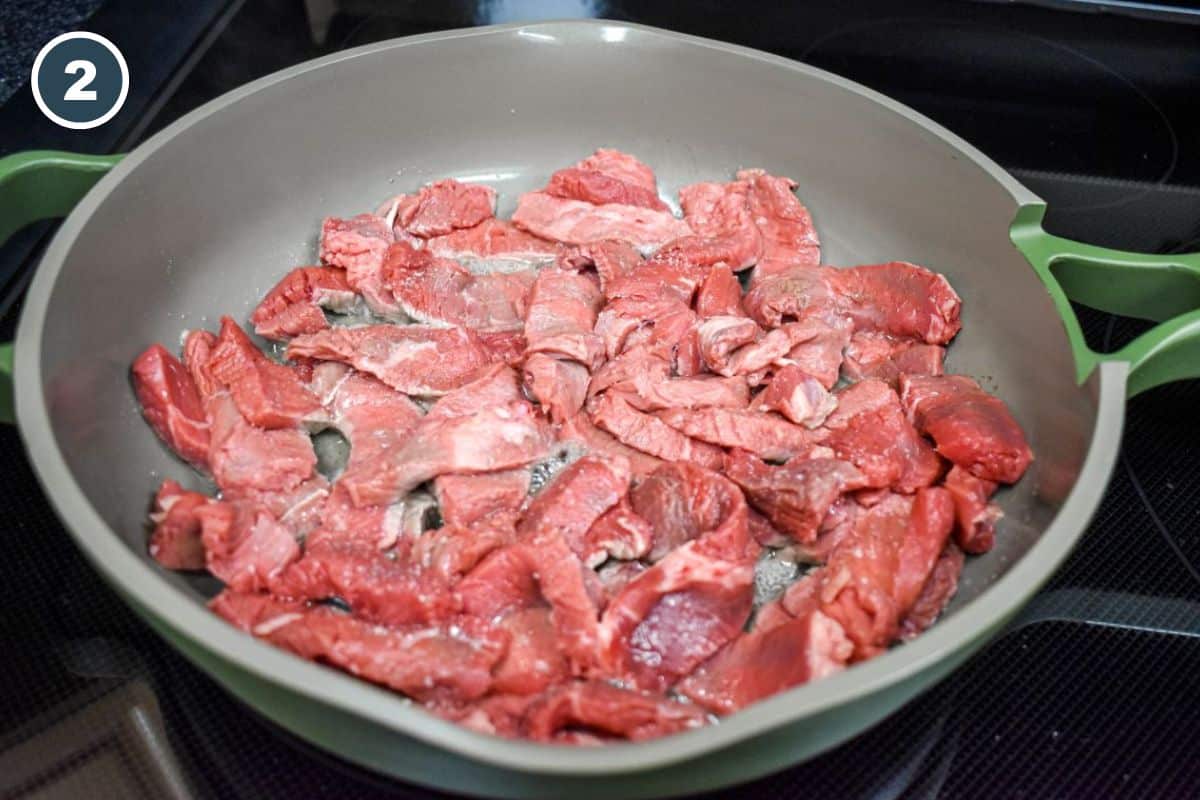 Thinly sliced raw beef cooking in a large skillet.