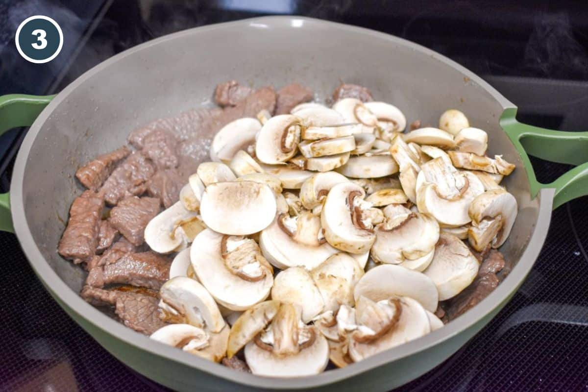Sliced mushrooms added to the skillet with partially cooked beef.