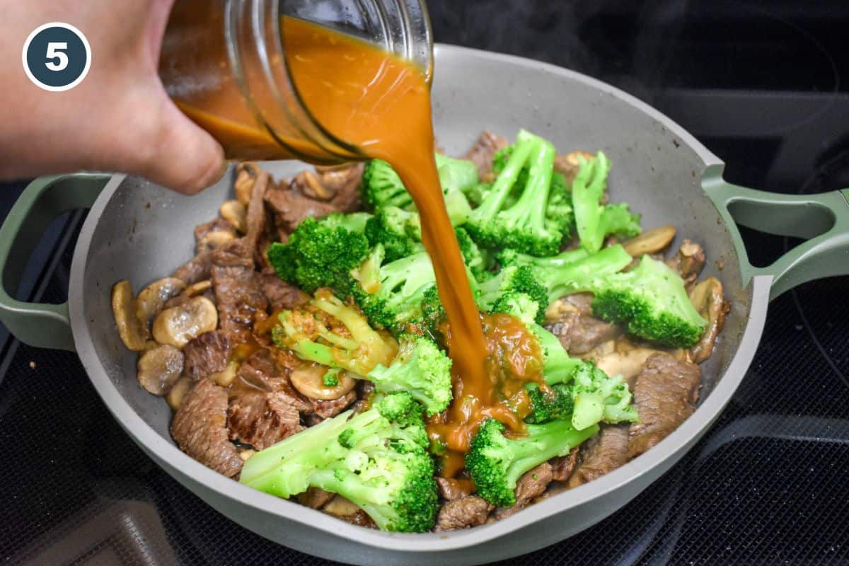 Sauce being poured from a jar into the skillet with beef, mushrooms, and broccoli.