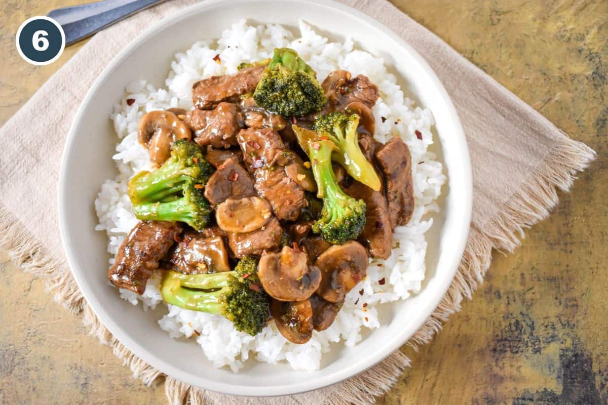 Finished beef, broccoli, and mushrooms served over white rice in a shallow bowl.