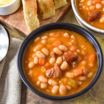Bowl of navy bean soup with carrots and smoked ham, served with sliced bread and butter on the side.