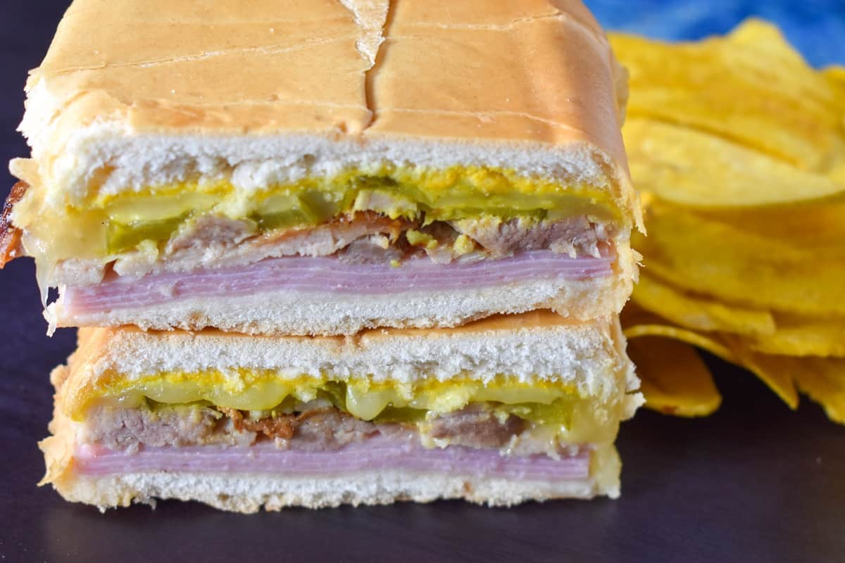 A close up image of the cuban sandwich displayed on a black surface with yellow plantain chips on the right hand side.